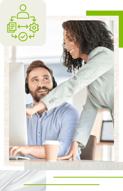 A woman in a light green blazer assists a person at a computer, providing guidance and support in an office setting.