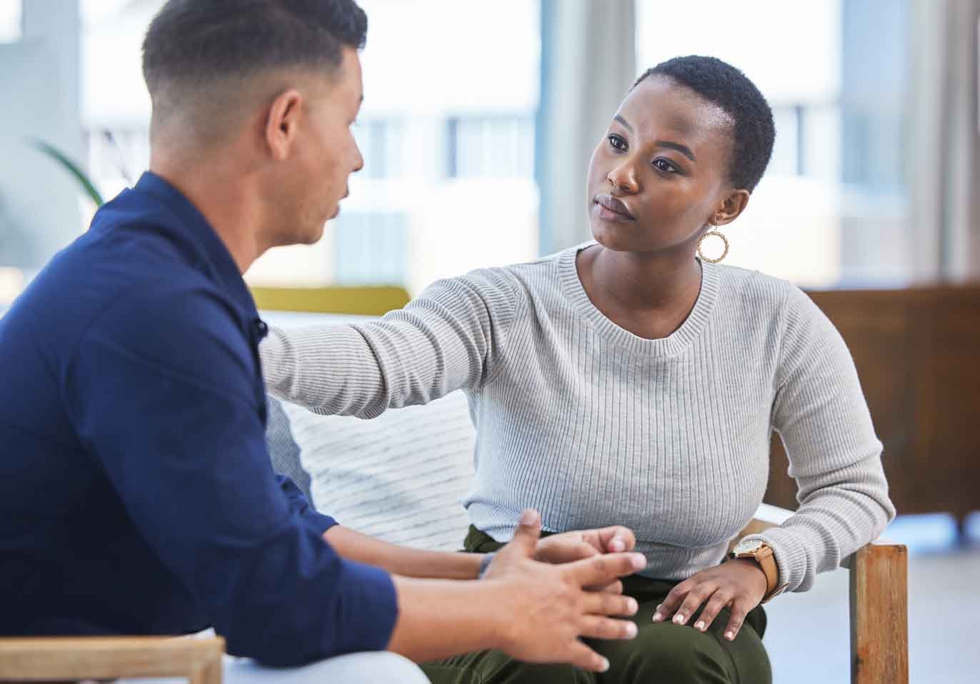 A seated woman gestures attentively during a conversation with a man, both engaged and focused in a cozy, modern setting.