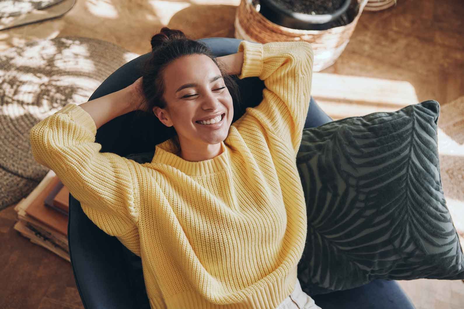 A person relaxes on a cozy chair, wearing a bright yellow sweater, with green cushions and sunlight streaming into a warm, inviting room.